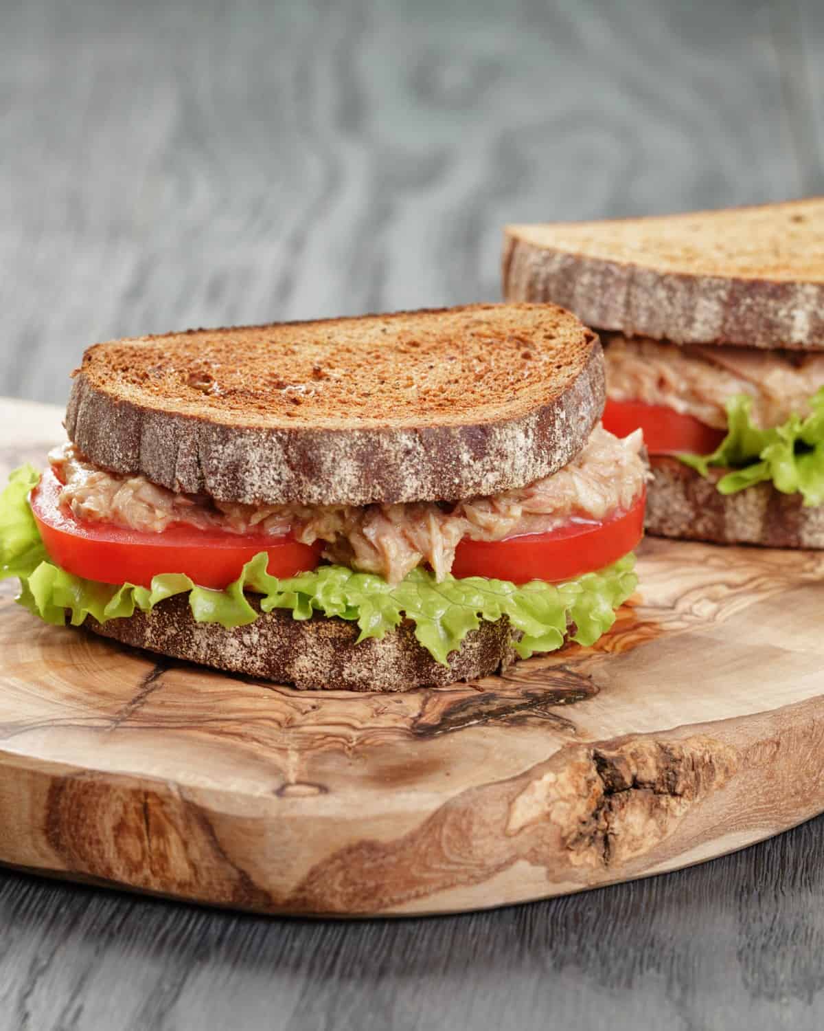 rye bread sandwich filled with tuna, tomatoes and salad.