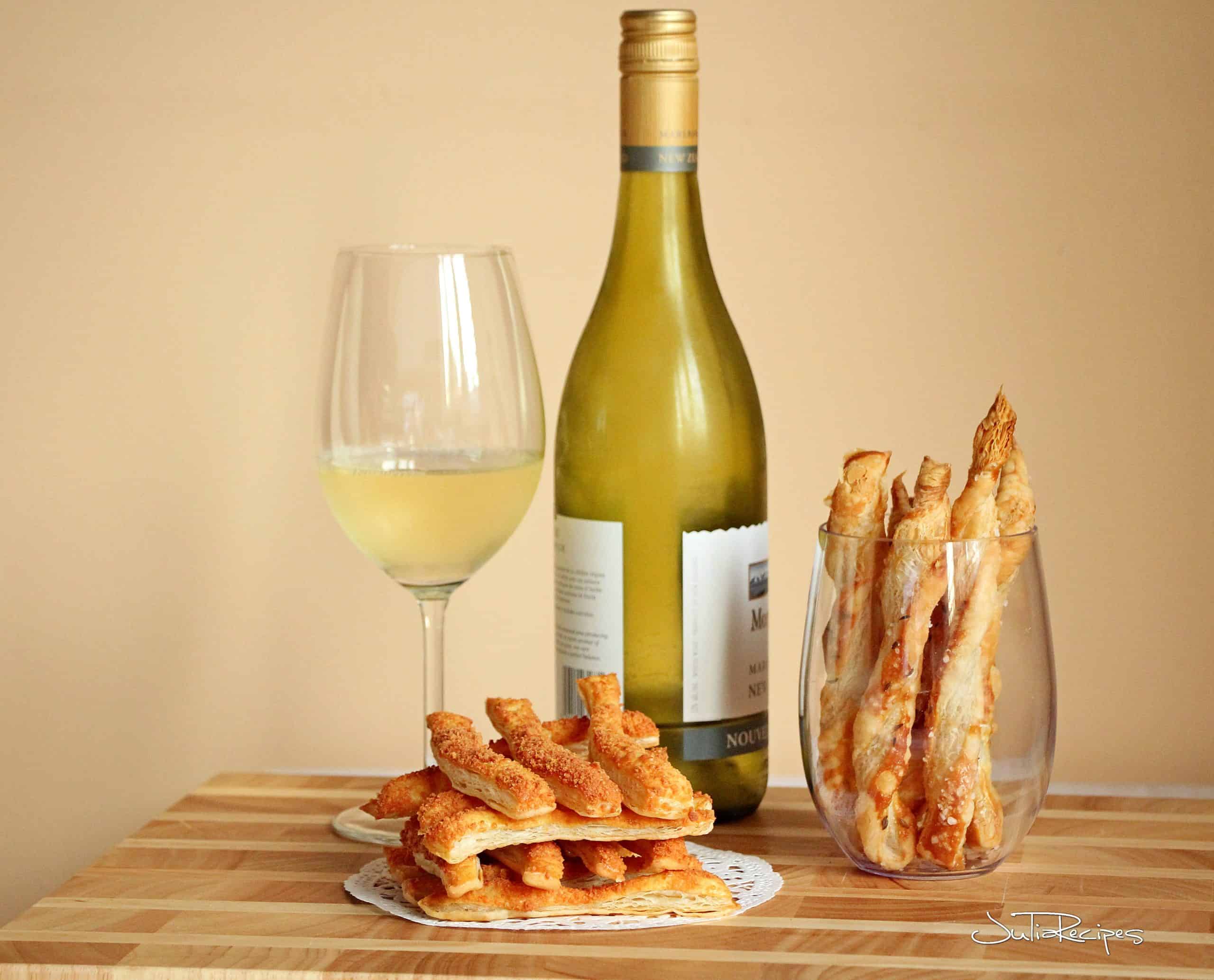 parmesan sticks from puff pastry in wine glass. In background white wine in glass and in bottle.