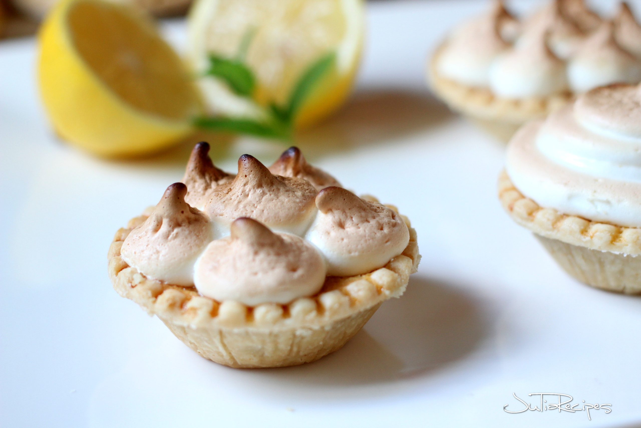 Small lemon tarts on white plate garnished with meringue