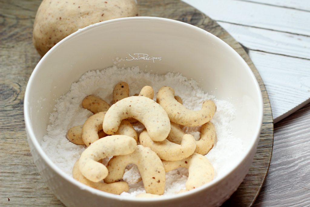 cookies in crescent shape in bowl of icing sugar
