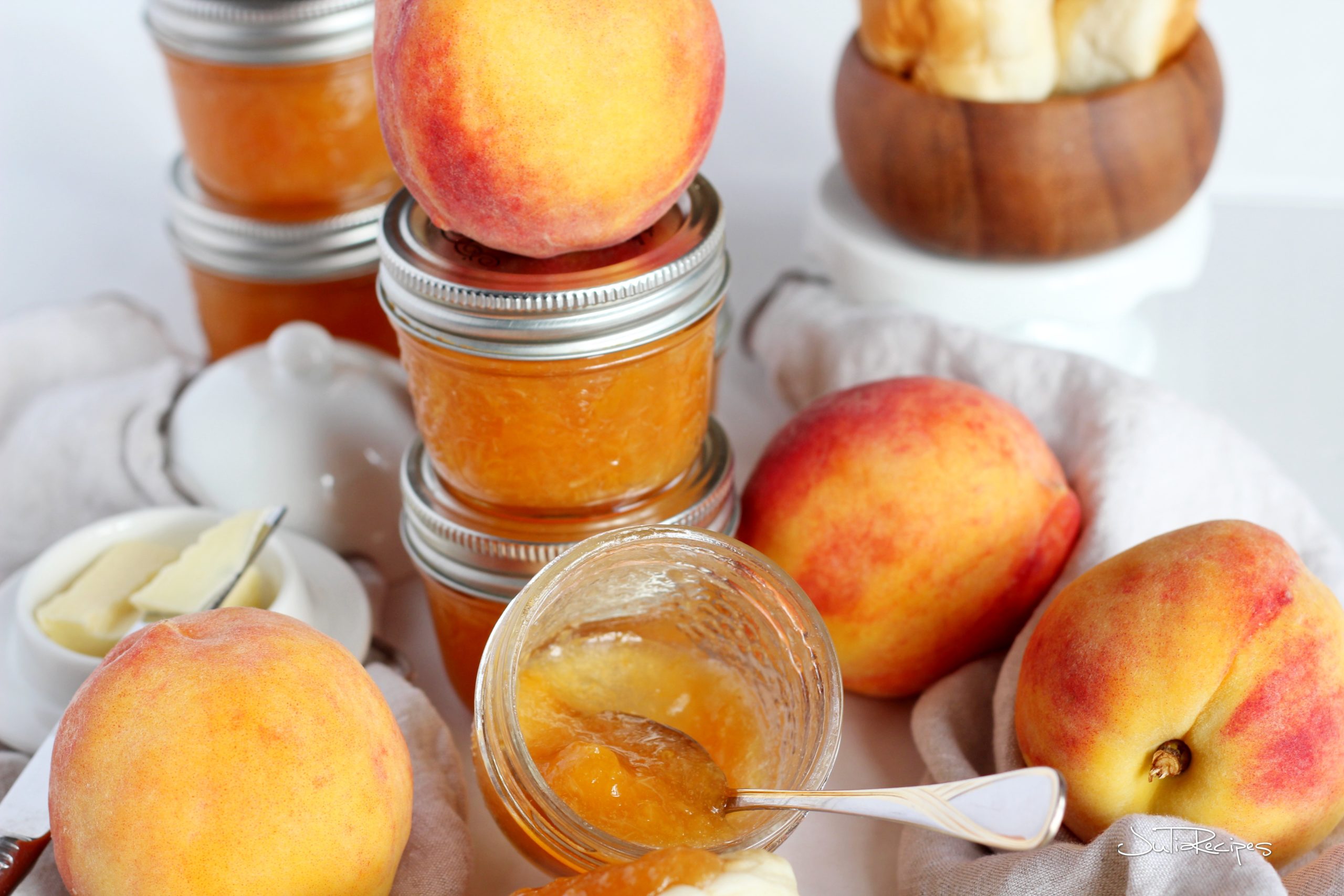 peach jam in jars with fresh large peaches around, one jar is open and jam is spooned out
