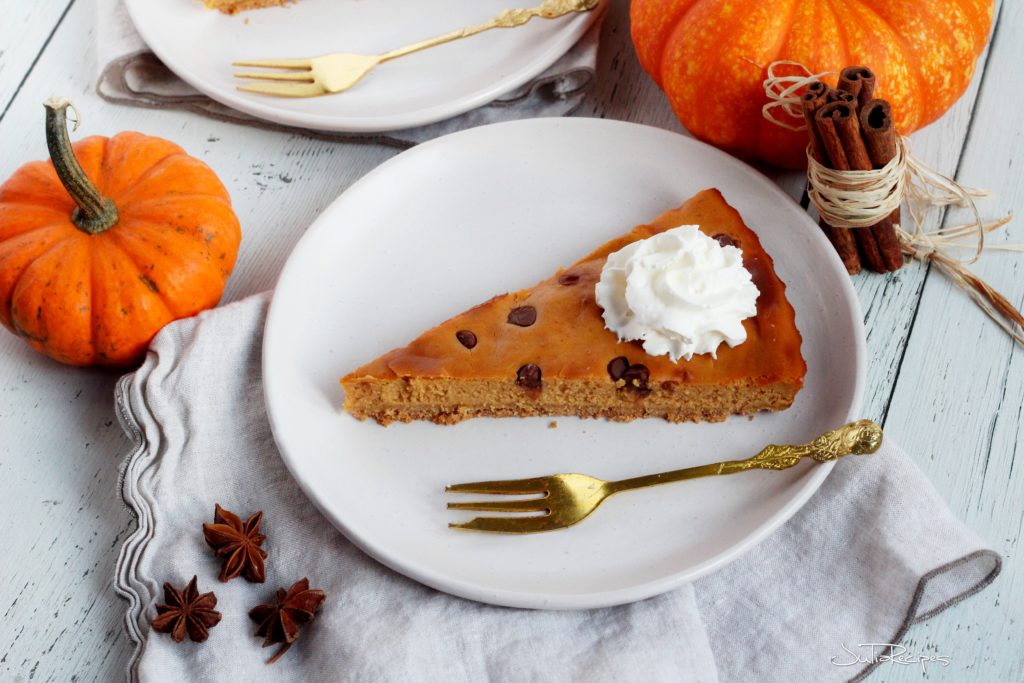Triangle slice of pumpkin spice cheesecake on white plate with orange mini pumpkins in the background