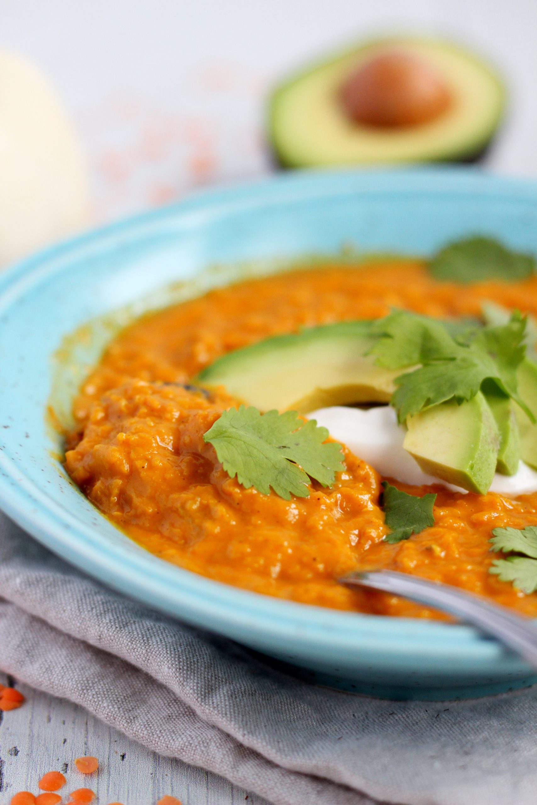 lentil curry in blue plate topped with avocado and cilantro
