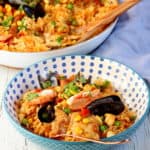 colorful rice with seafood on blue dotted plate with paella pan in background