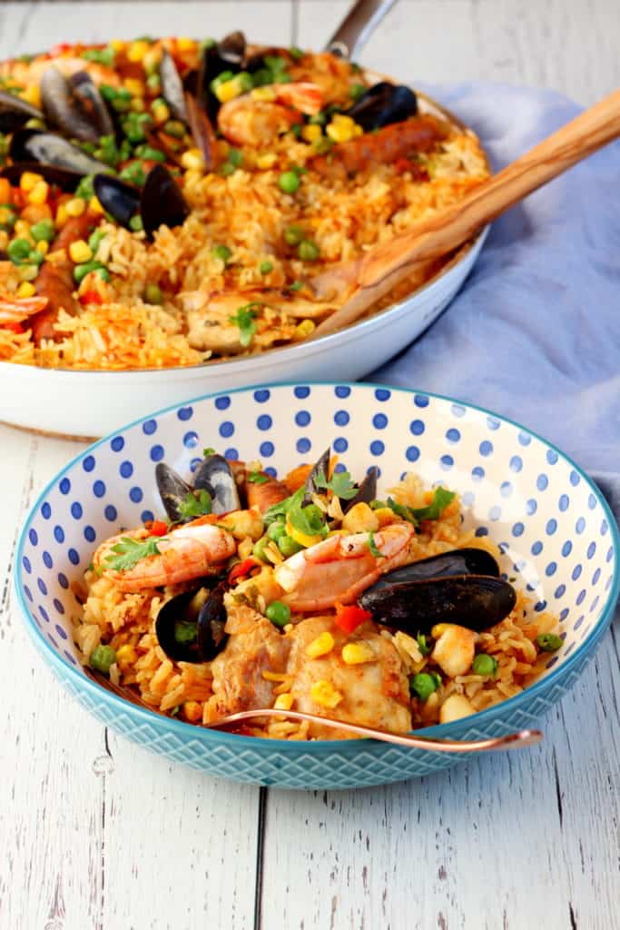 colorful rice with seafood on blue dotted plate with paella pan in background