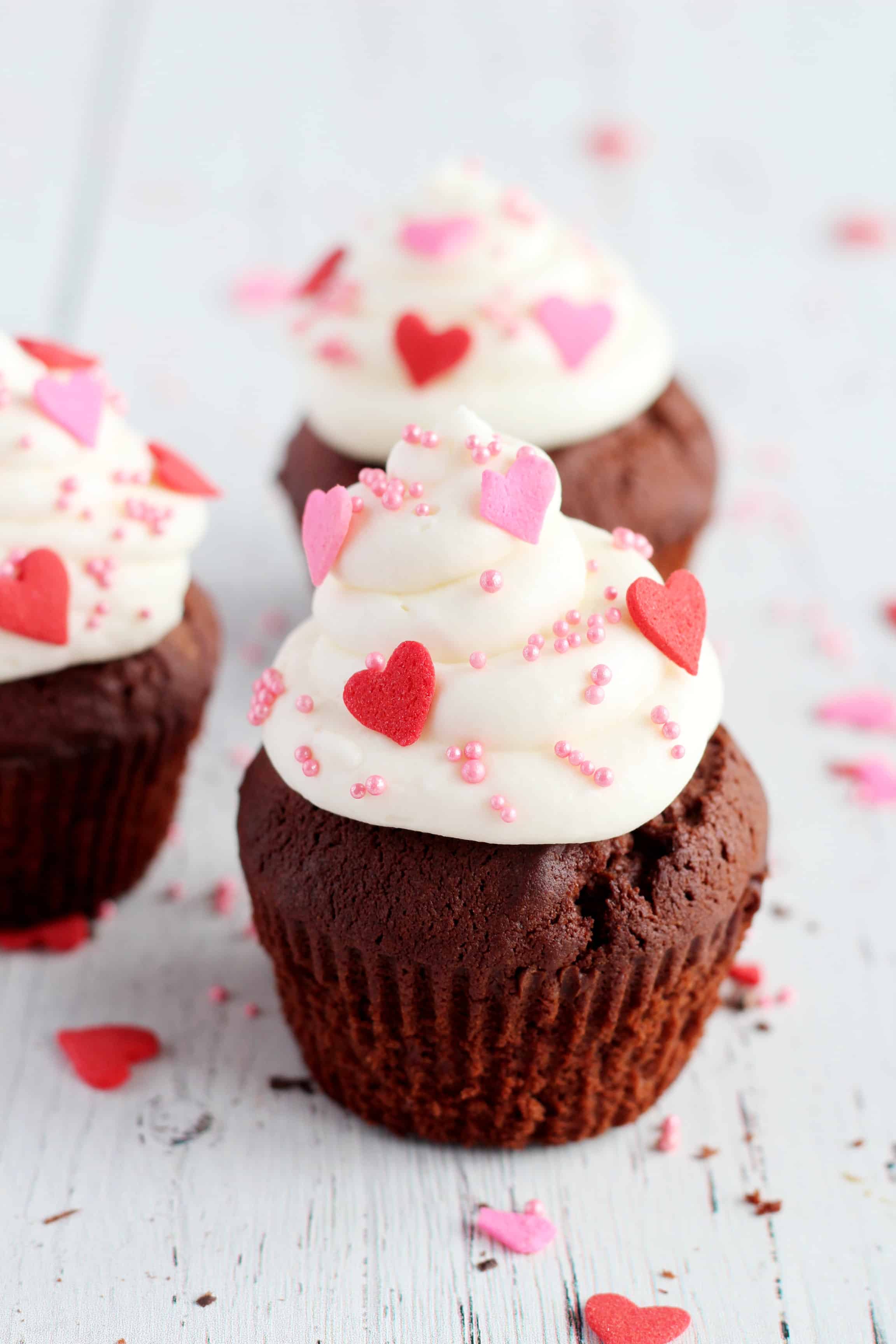 chocolate cupcakes with whipped cream on top and decorated with red and pink hearts