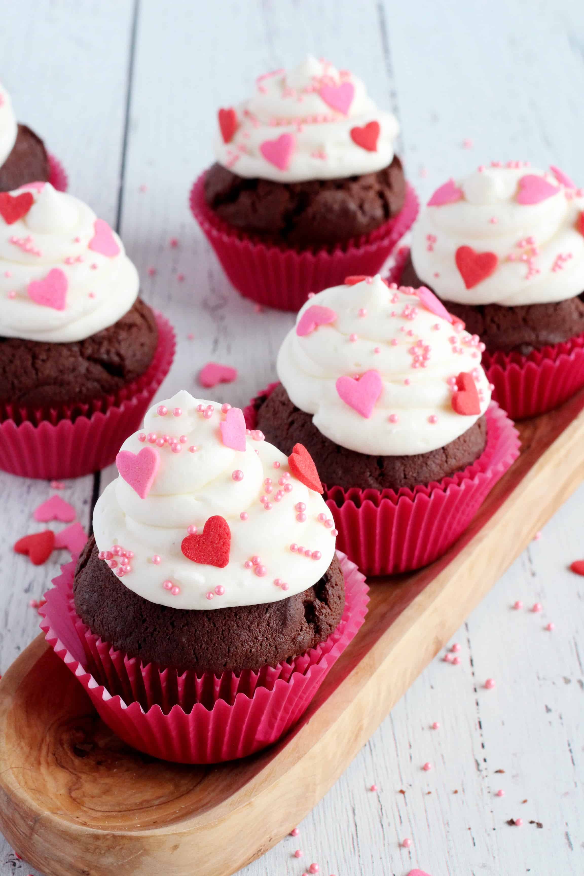 chocolate cupcakes topped with whipped cream and decorated with red and pink sprinkles