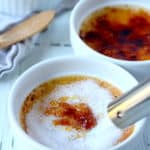 creamy creme brule in white ramekin with sugar being melted by torch another ramekin with creme brulee in background