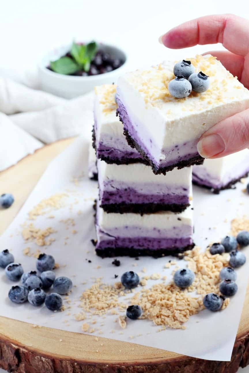 Blueberry cheesecake squares stacked on each other, one square in hand holding and focused on camera