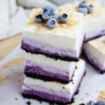 Blueberry cheesecake squares stacked on each other with other blueberry squares behind