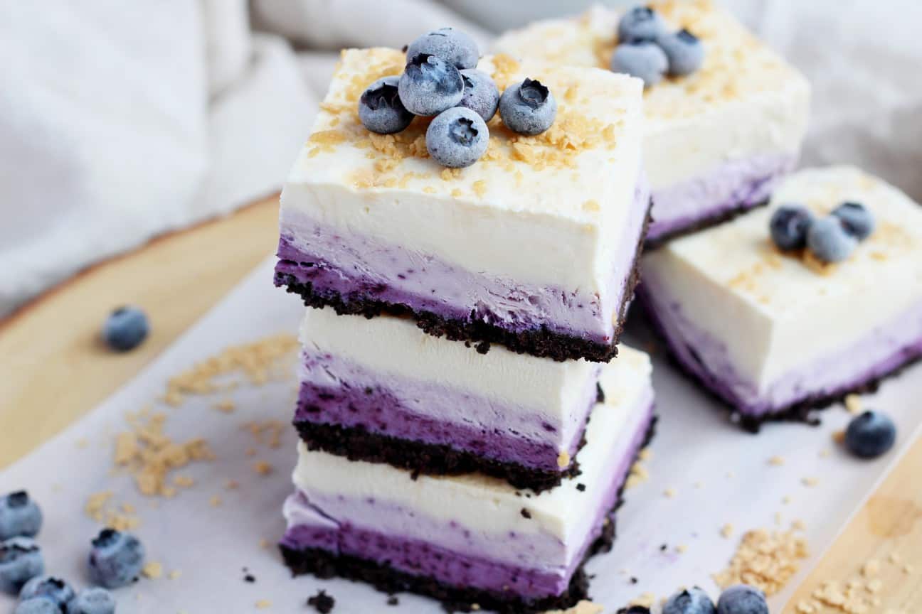 Blueberry cheesecake squares stacked on each other with other blueberry squares behind