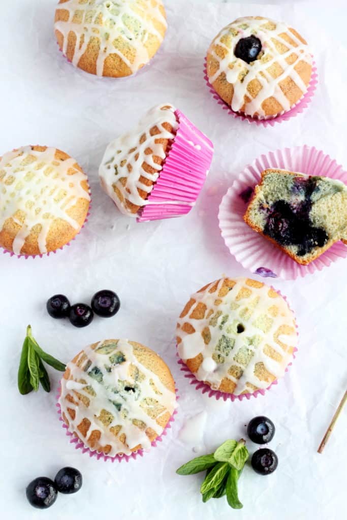 Six blueberry muffins with lemon glaze laying in parchment paper