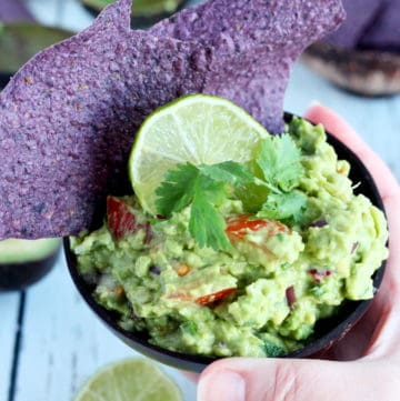 Simple guacamole dip inside woden bowl with tortilla chips and slice of lime