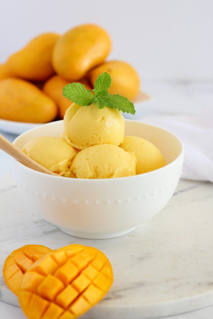mango sherbet in white bowl with whole mangoes on plate in the background