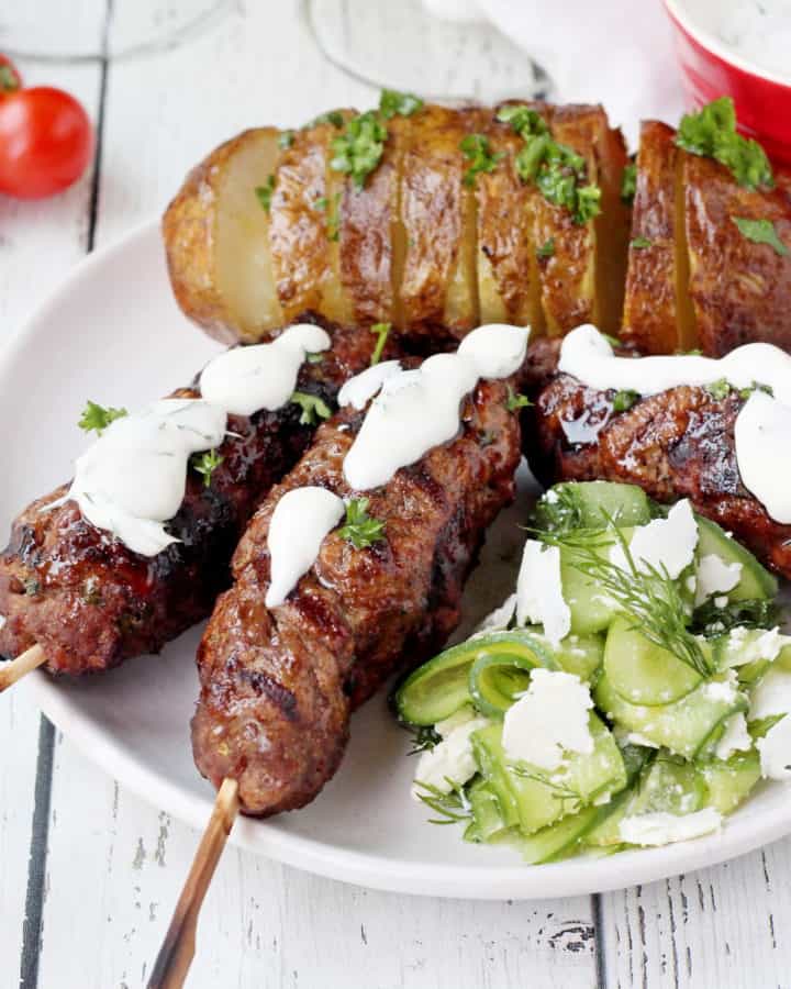 close up of bbq'd kebaba with roasted potatoes and cucumber salad with feta cheese
