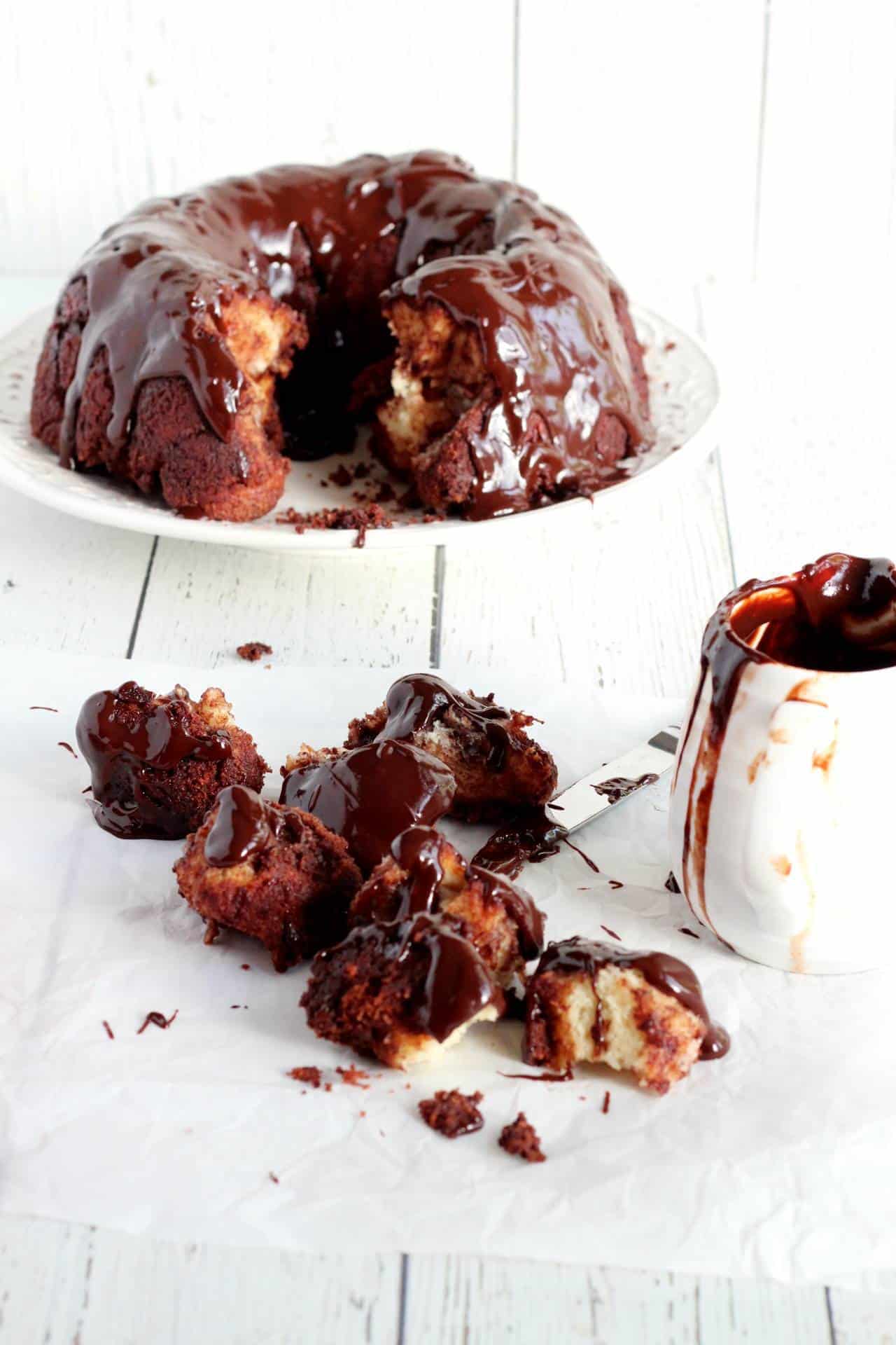 Chocolate bundt monkey bread laying in the background. Small pieces of baked monkey bread covered in messy chocolate glaze layed on white parchemnt paper