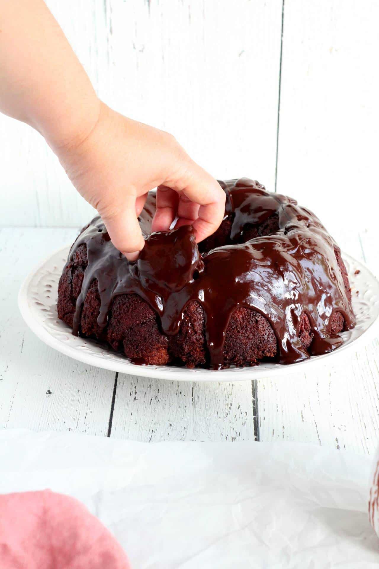 Hand grabbing first piece of pull apart chocolate bread from white plate
