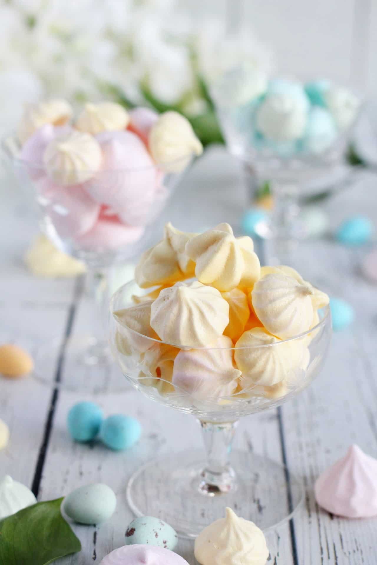 Yellow meringues in champagne glass with other meringues around of pastel colors