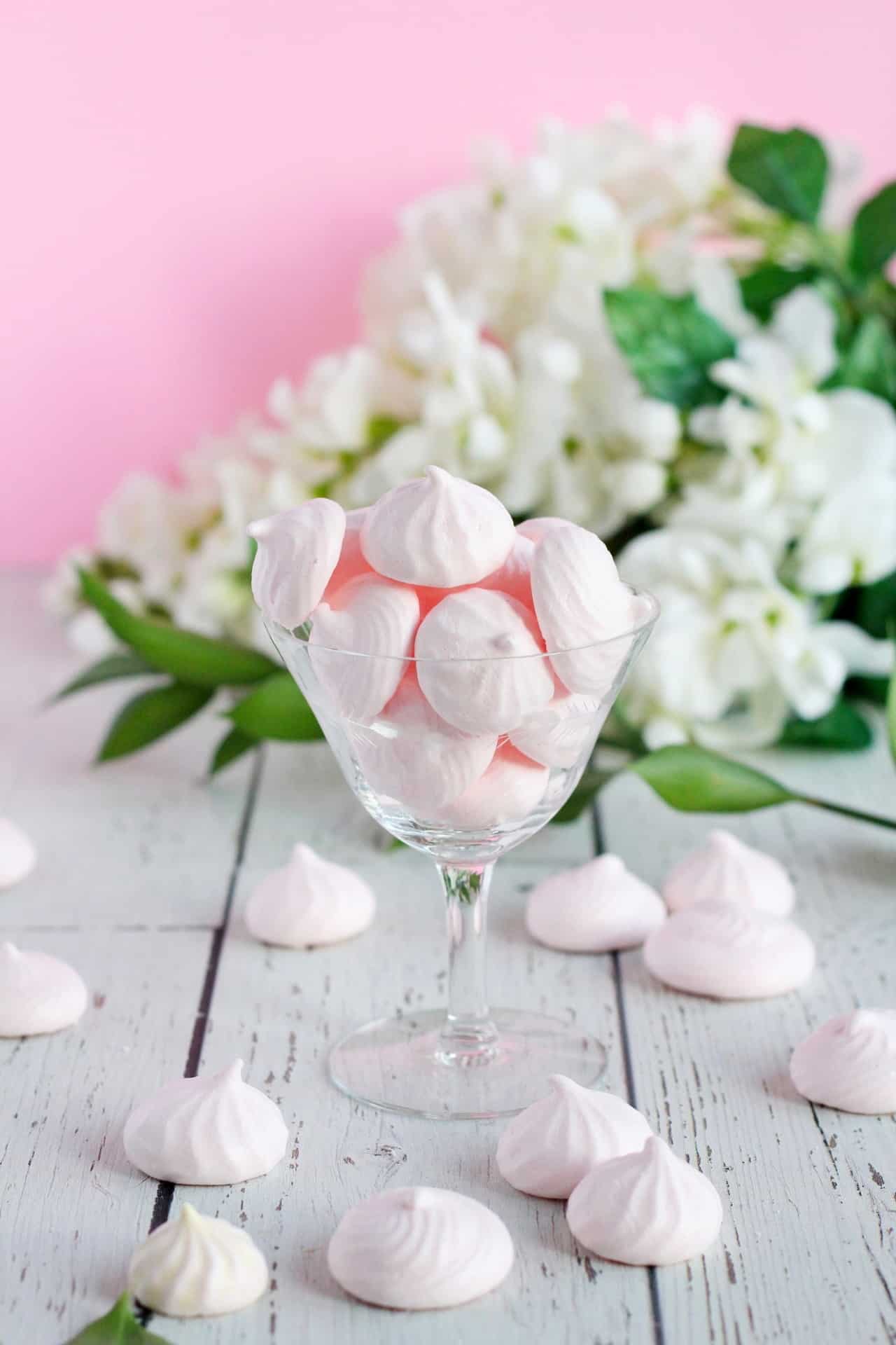 pink meringues in mini size inside vintage champagne glass with white flowers behind