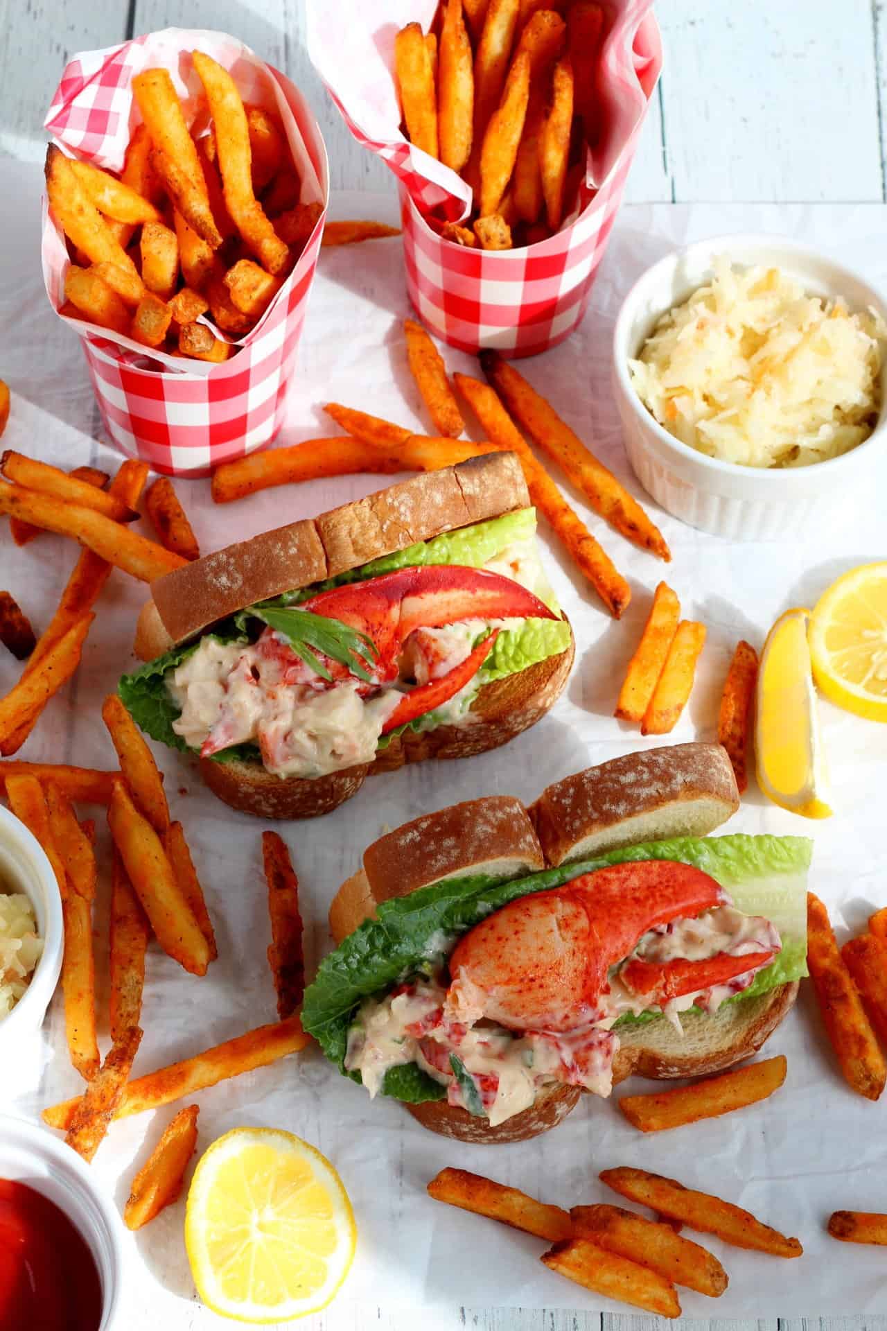 two lobster rolls in hot dog buns with sweet potato fries laying around