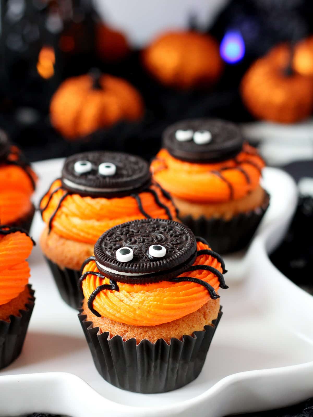 close up of vanilla cupcakes with orange frosting and oreo spiders on top
