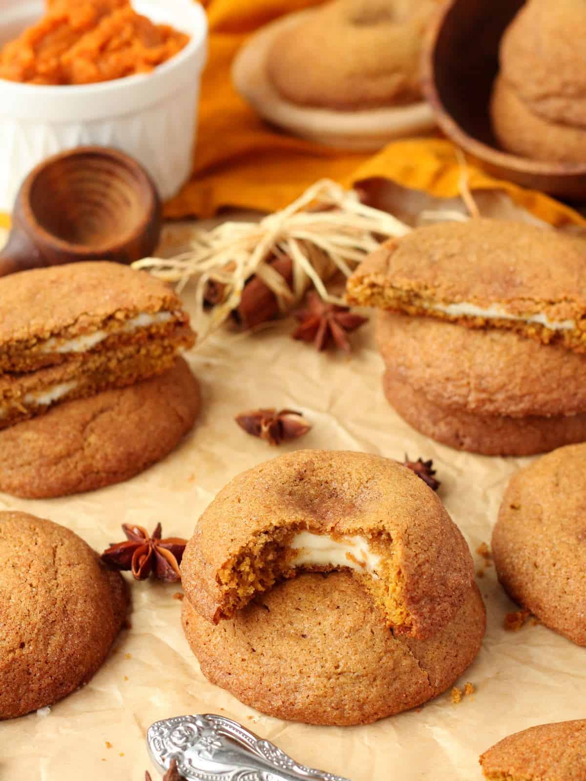 warm pumpkin cookies filled with cream cheese, scattered on a brown parchment paper with pumpkin puree and fall decoration in the background