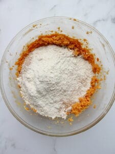 dry ingredients tossed into wet ingredients for pumpkin cookies in transparent bowl