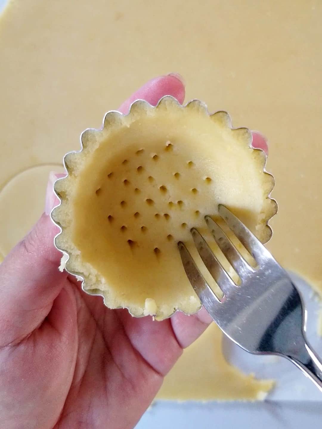 dough in mini tart mould being pricked by the fork
