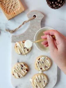 drizzling cranberry cookies with white chocolate on white marble board with golden spoon