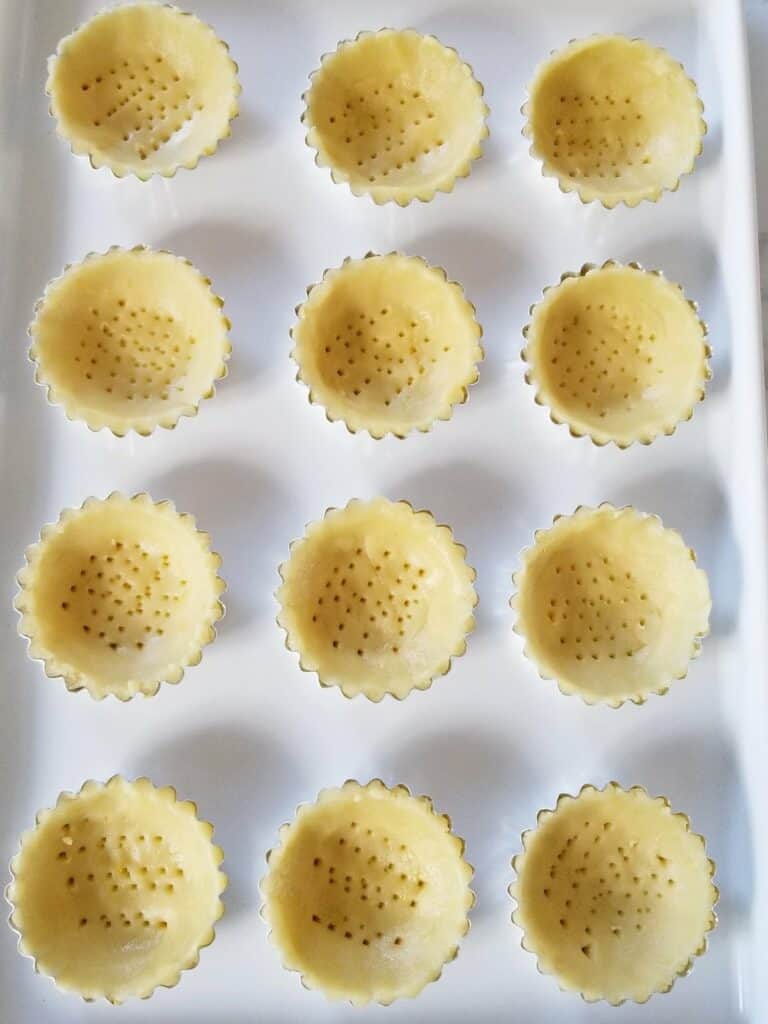 twelve mini tart shell moulds filled with dough and placed together on white baking sheet