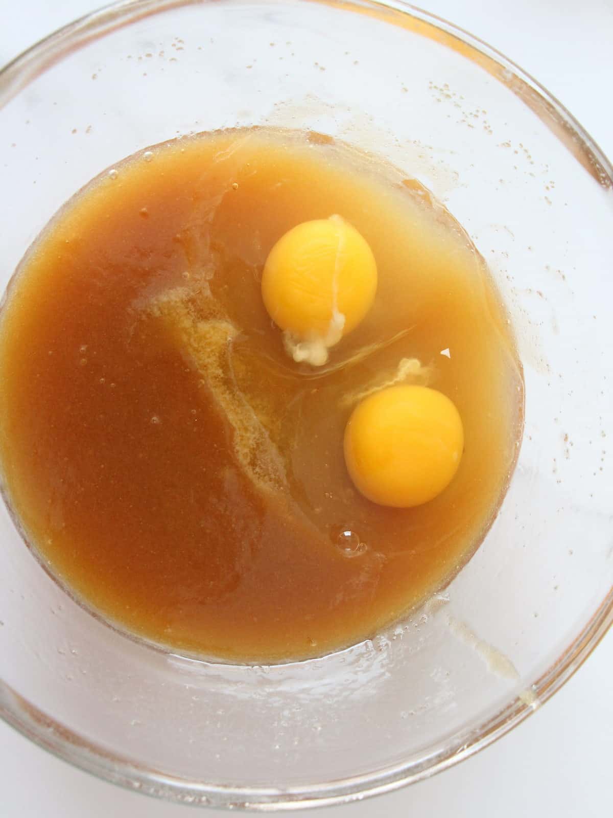 two whole cracked eggs inside melted butter with brown sugar getting ready to be mixed