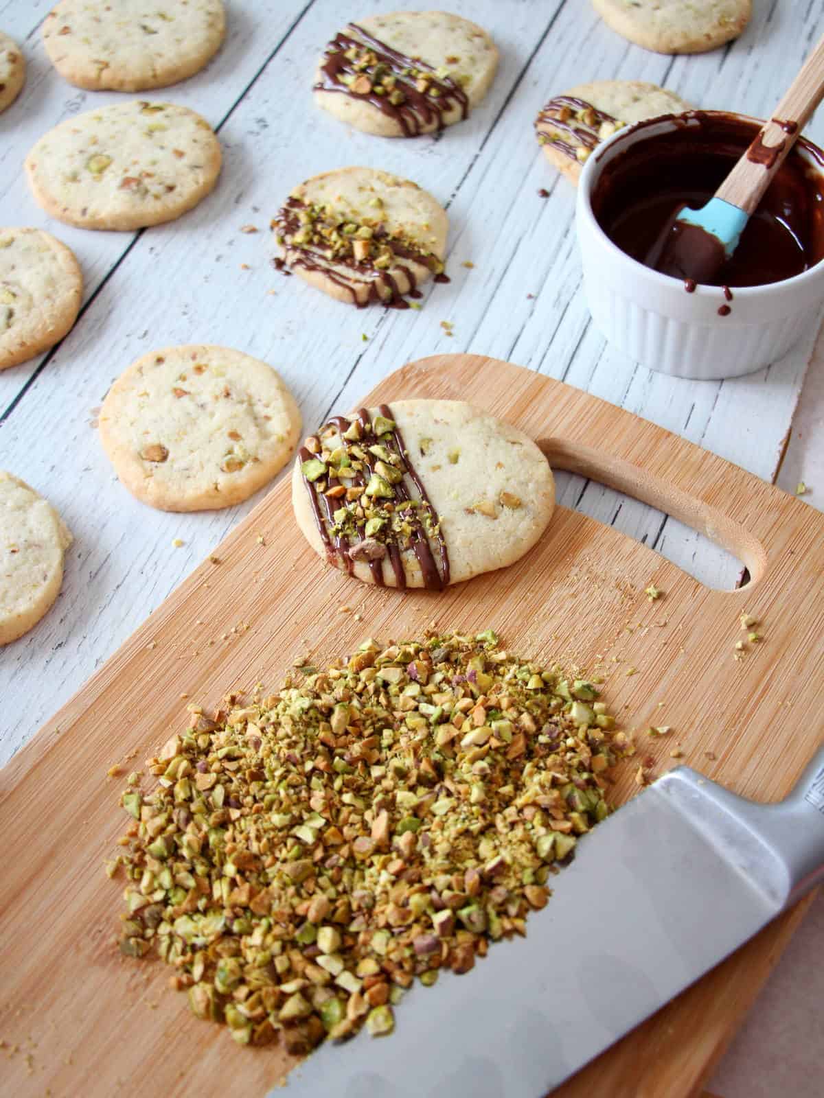 roughly chopped pistachios on wooden board next to shortbrad cookies