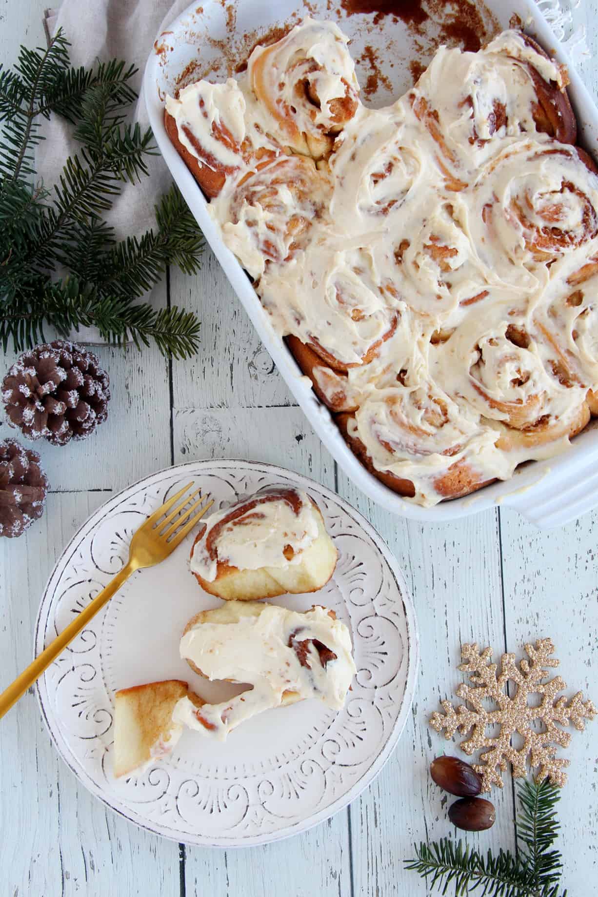 eggnog cinnamon rolls in white pan. One cinnamon roll on a plate with golden fork
