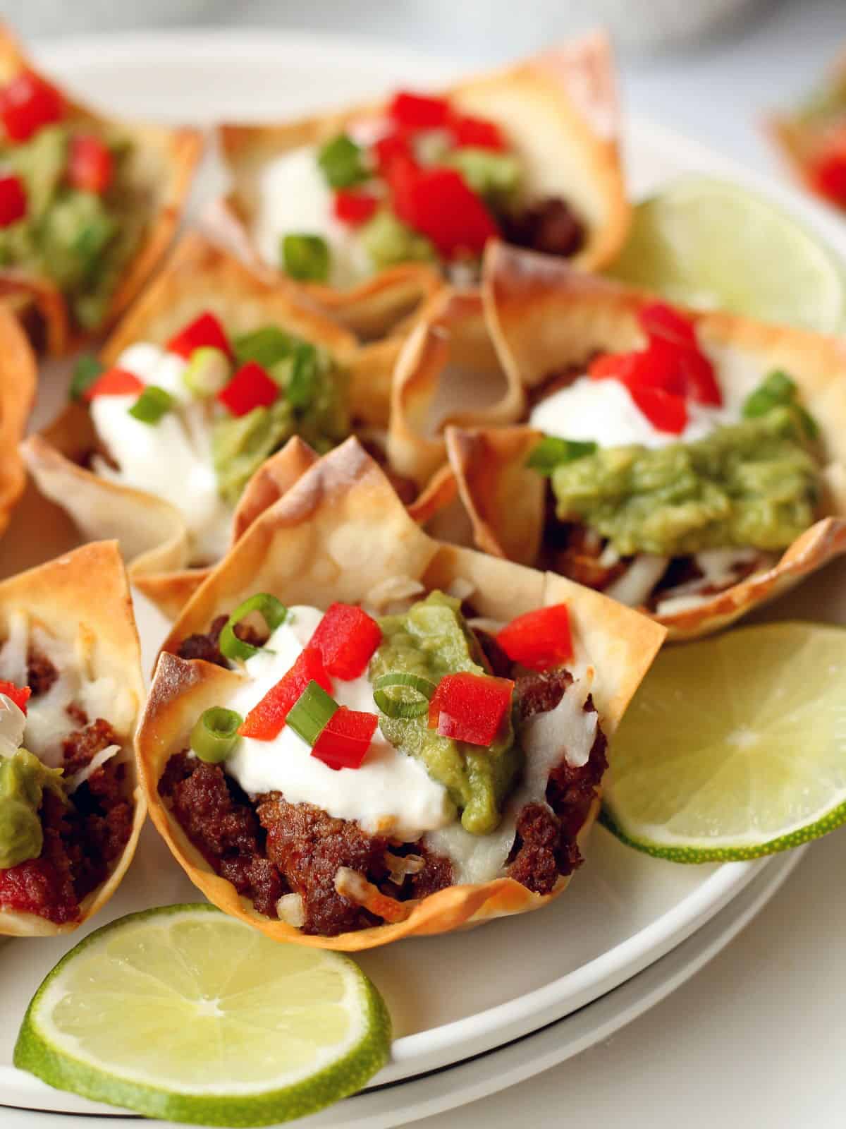 close up of taco cups filled with beef and topped with sour cream and guacamole