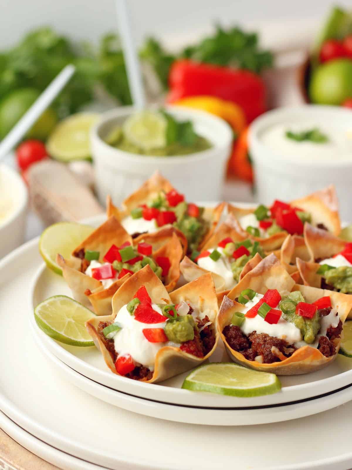 close up on taco cups filled with beef, cheese, sour cream, guacamole and topped with chives and bell pepper pieces
