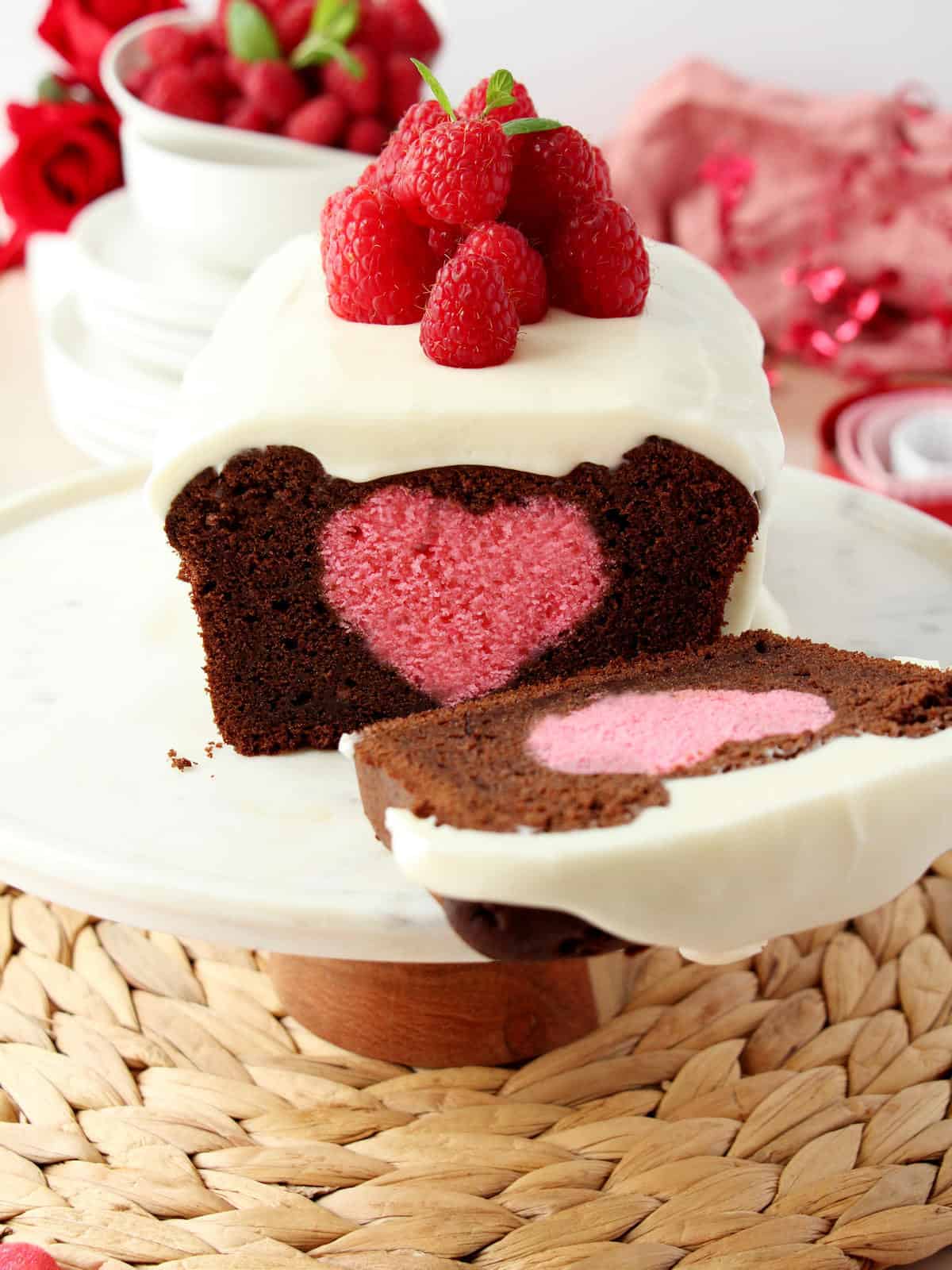 chocolate pound cake with pink hidden heart on marble stand, one slice laying on the side. Pink background with Valentine themed decoration.