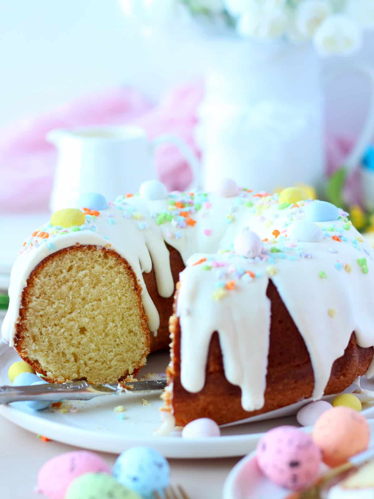 Bundt cake cut in the middle with few sliced mising. Easter decorated bundt cake with cream cheese on top.