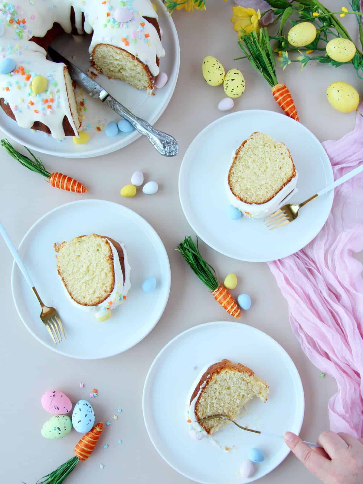 sliced of bundt cake on white plates and with white forks. Easter decoration in the background
