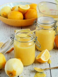 two mason jars filled with lemon curd, lemons around cut in quarters.