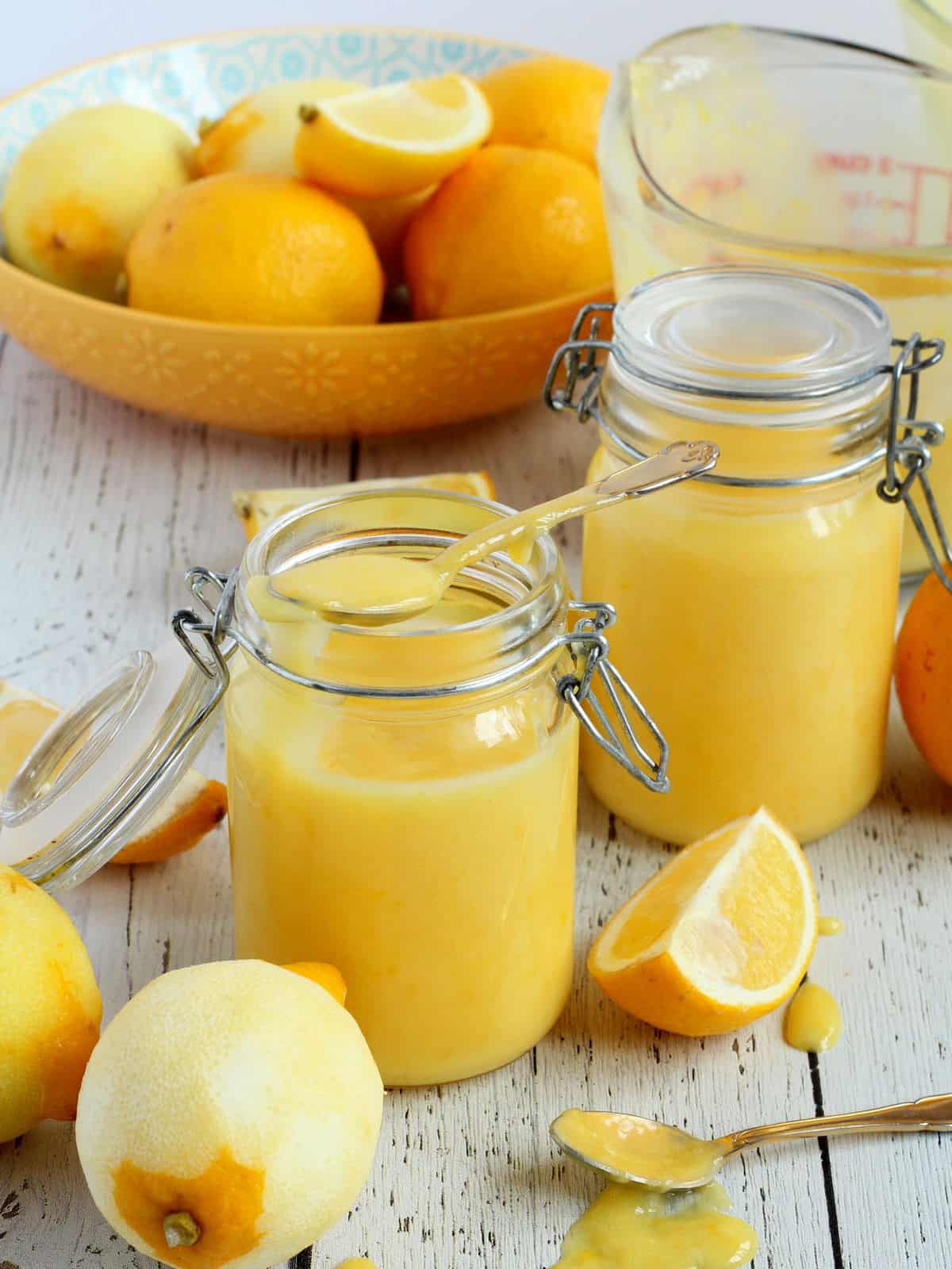 two mason jars filled with lemon butter, lemons around cut in quarters.